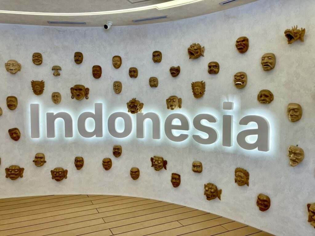 インドネシア館の展示壁。様々な表情の伝統的な木彫りの仮面が「Indonesia」のロゴを囲むように並べられている。文化の多様性を感じるデザイン。