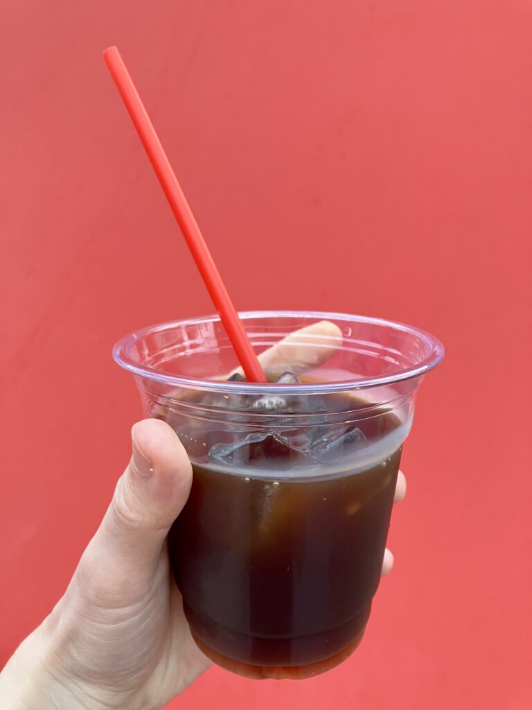 オマーン館で提供されたアイスコーヒー。赤い背景と赤いストローが印象的で、透明なカップに注がれたコーヒーが美しく映える